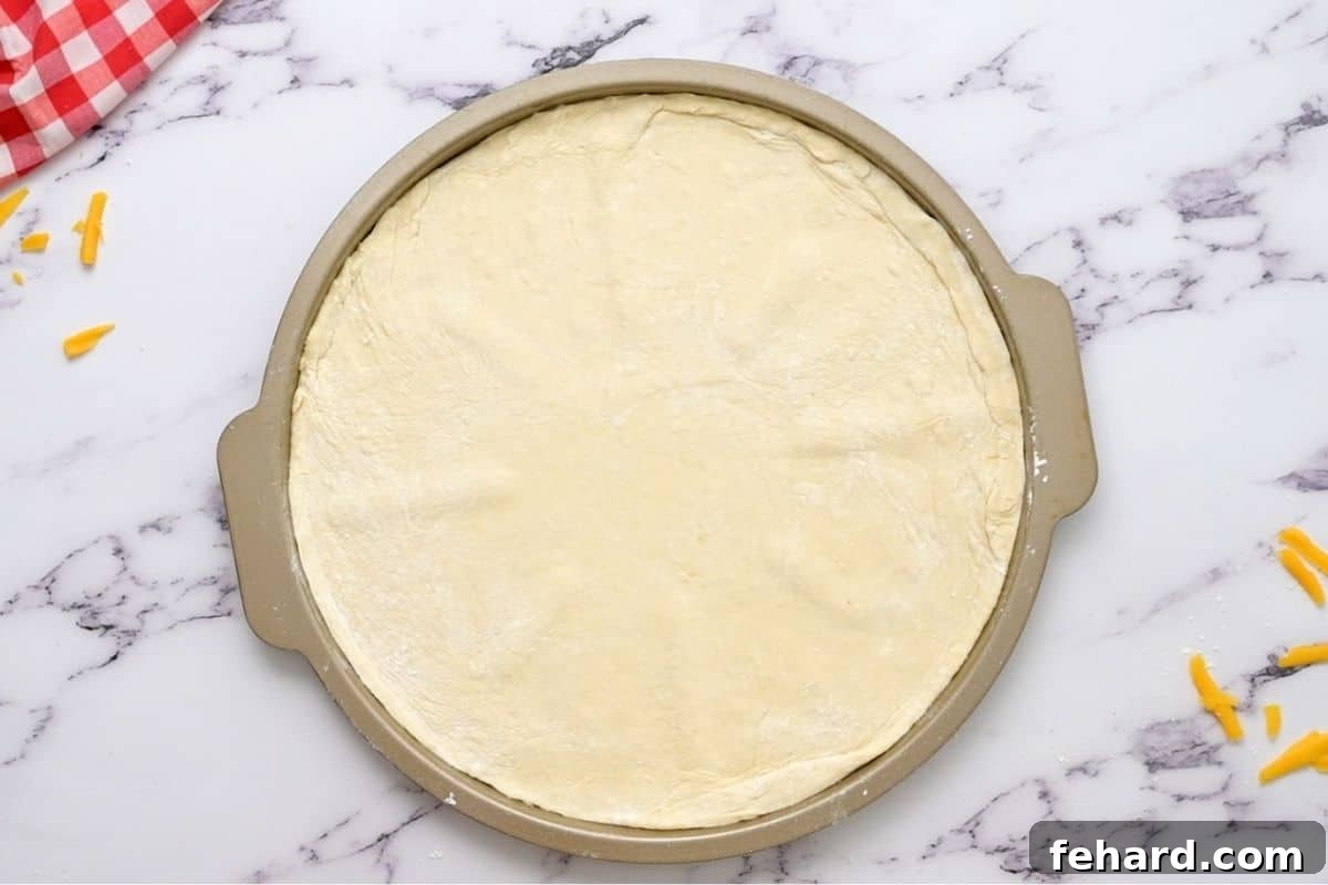 Preparing the pizza dough for the ultimate Taco Pizza Pizza dough perfectly rolled out and placed onto a pizza pan, its smooth surface ready for the layers of delicious toppings.