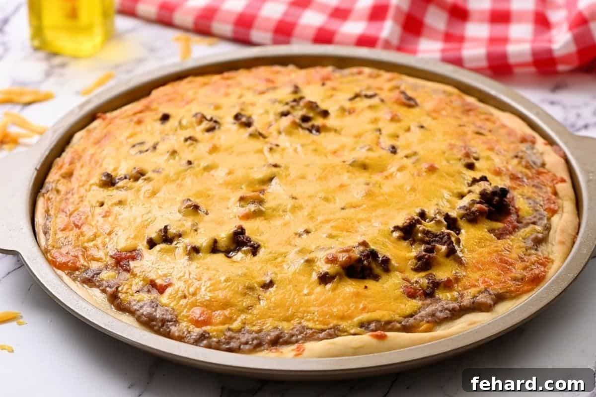Easy Baked Taco Pizza - fresh from the oven A freshly baked taco pizza resting on a round pizza pan, featuring beautifully melted and bubbly cheese, and a perfectly golden, crispy crust.