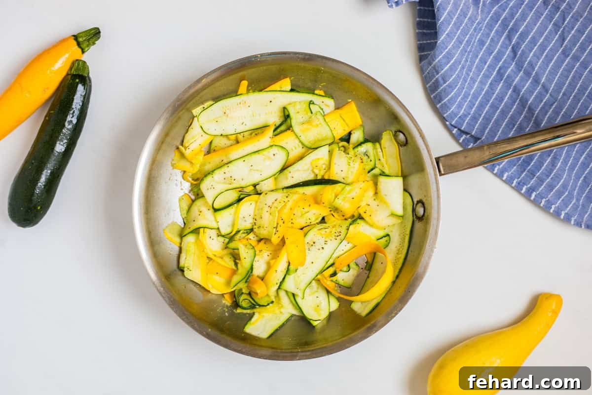 Sauteed Squash and Zucchini Quick Recipe Close-up shot of sautéed ribbons of bright summer squash in a small stainless steel frying pan, lightly seasoned and garnished with fresh parsley.
