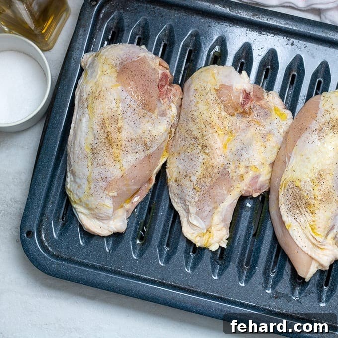 Raw split chicken breast on a baking sheet, seasoned with salt and pepper, ready for roasting.
