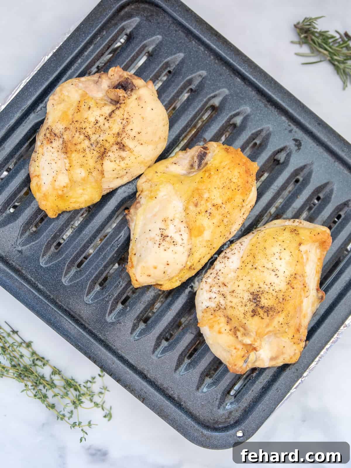 Freshly roasted split chicken breast on a broiler pan, garnished with fresh thyme, ready to be served.