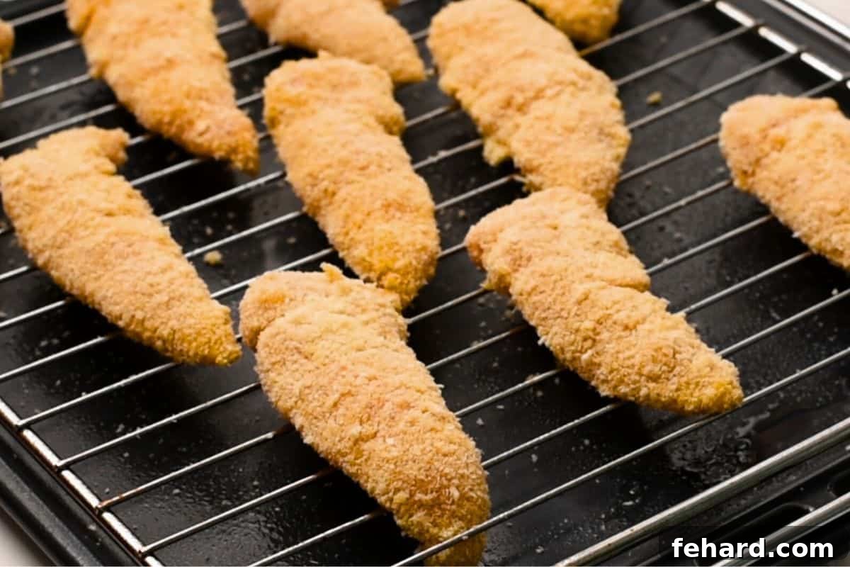 Crispy Chicken Tenders on Rack Perfectly baked crispy chicken tenders cooling on a wire rack positioned over a baking sheet, showcasing their golden and crunchy texture.