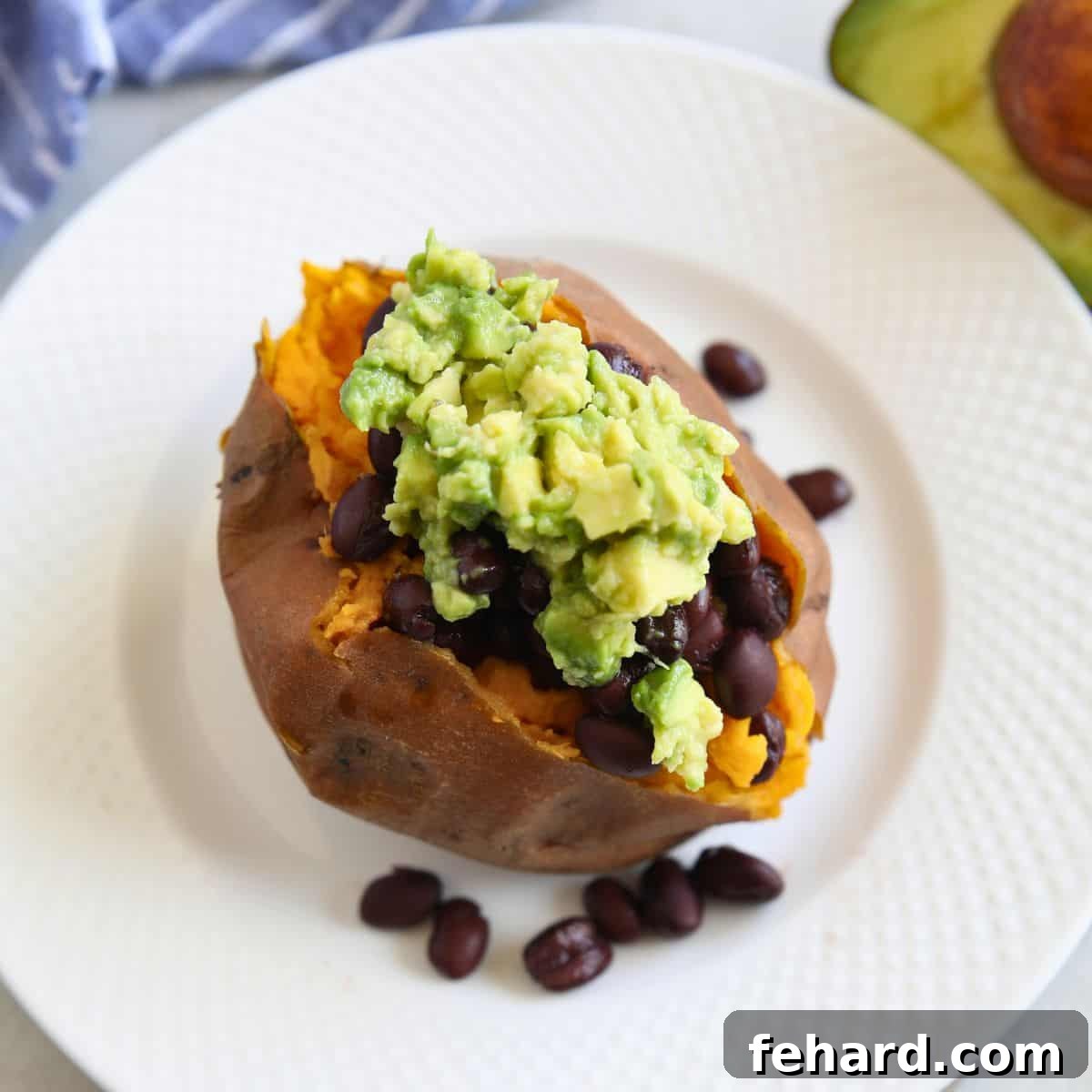 A perfectly baked sweet potato on a plate, generously topped with savory black beans and creamy avocado.