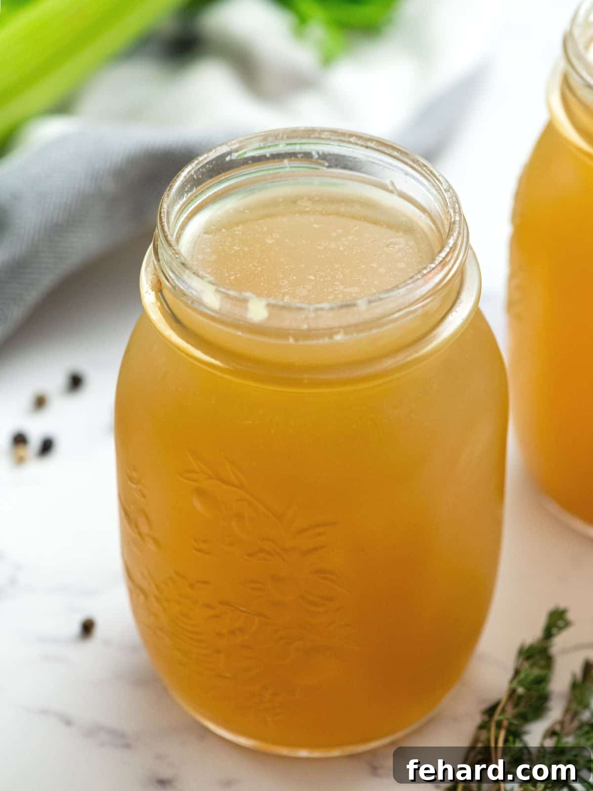 Jar of homemade chicken broth next to fresh thyme, ready for use or storage.