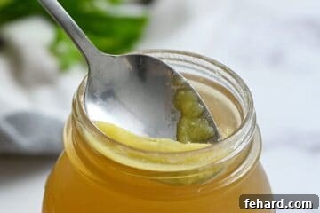A spoon skimming solidified fat from the top of chilled chicken stock stored in a glass jar.