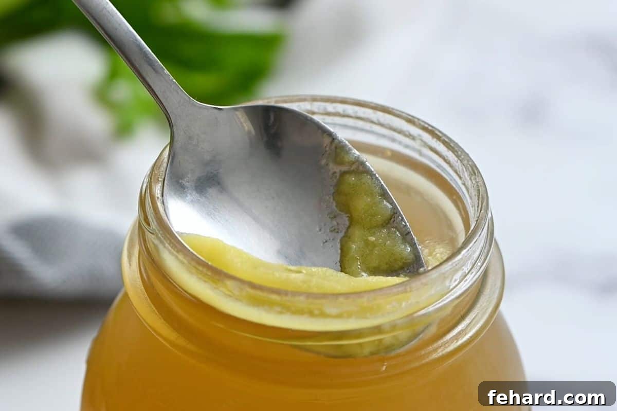 A spoon skimming solidified fat from the top of chilled homemade chicken stock in a glass jar.