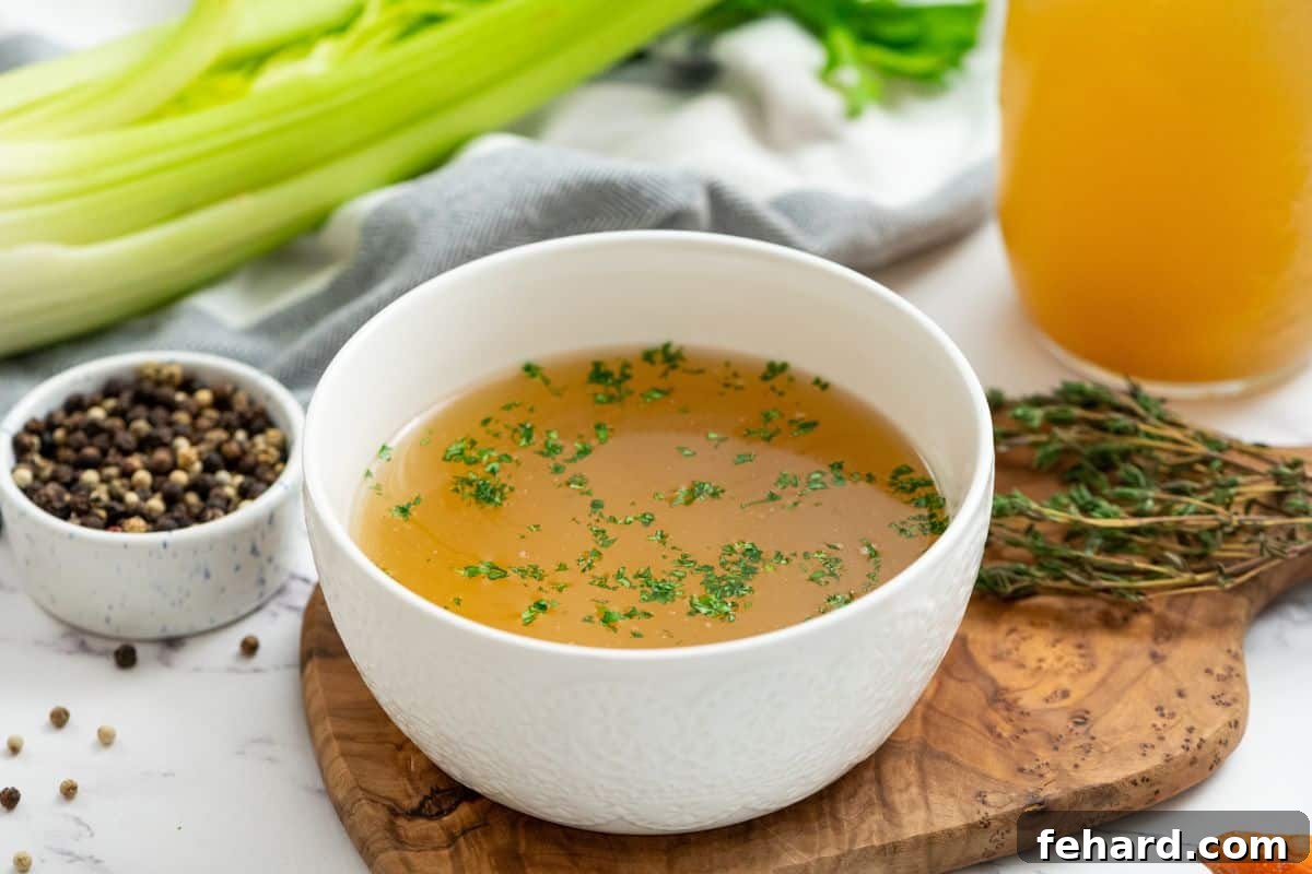 Bowl of homemade chicken stock topped with minced parsley, indicating its readiness for use.