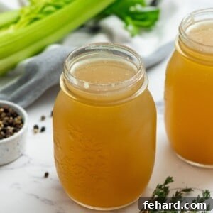 Two jars of homemade chicken stock next to peppercorns and thyme, representing the finished product.
