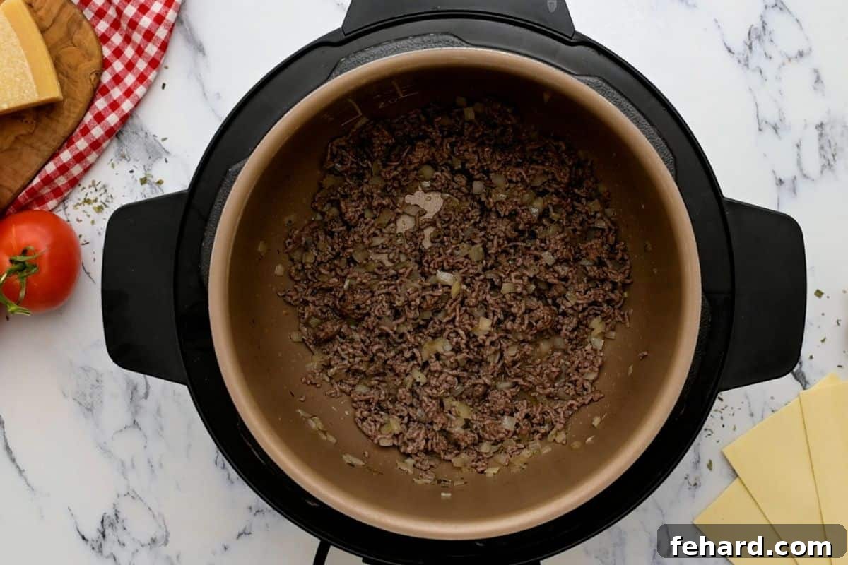 Ground beef and minced onion being sautéed together in the inner pot of an Instant Pot.
