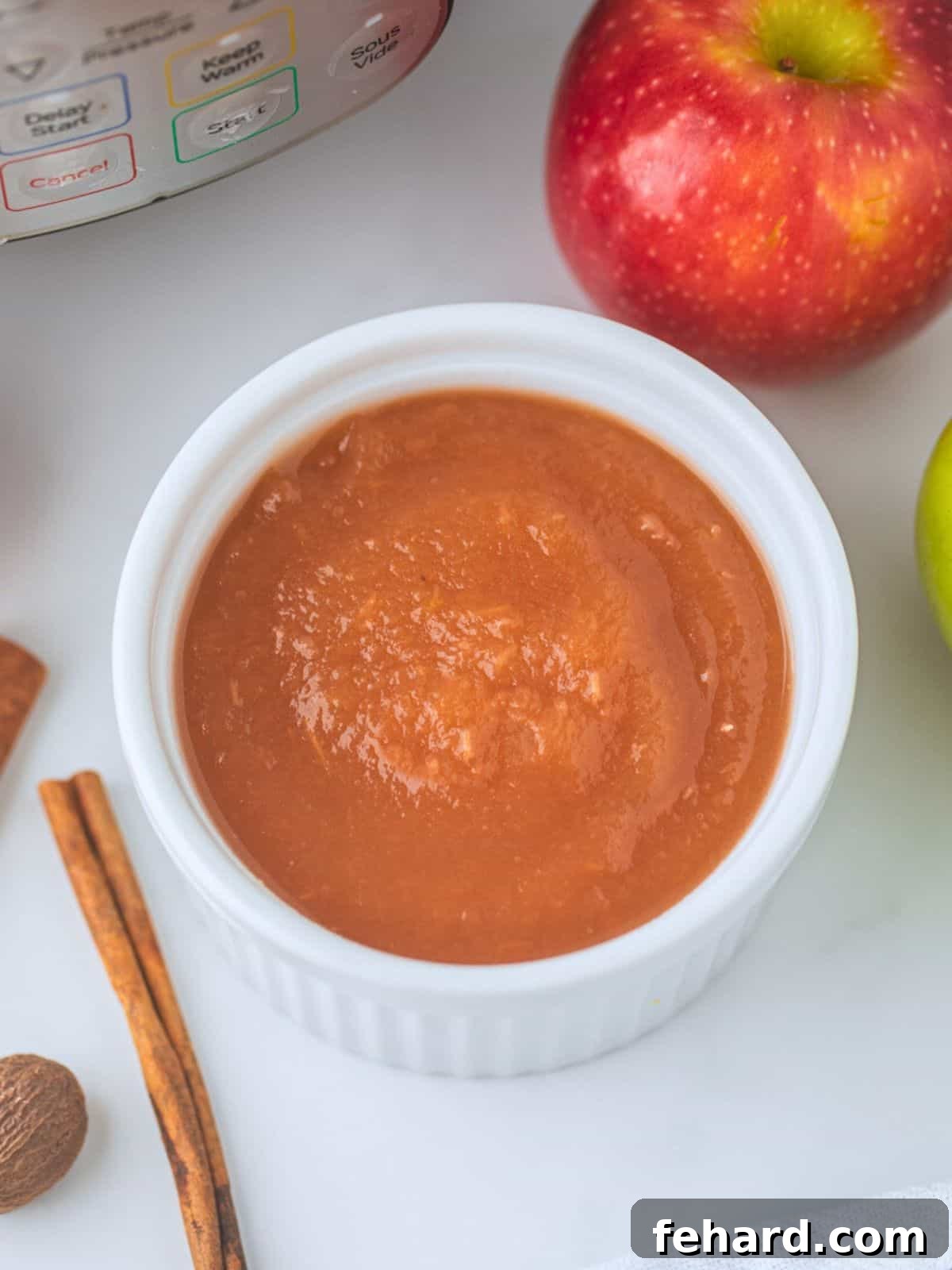Bowl of homemade no peel Instant Pot applesauce next to sweet apples and cinnamon sticks.