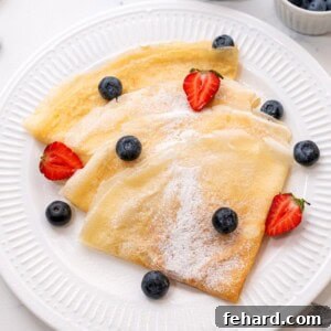 Golden brown crepes on a white plate with fresh berries.