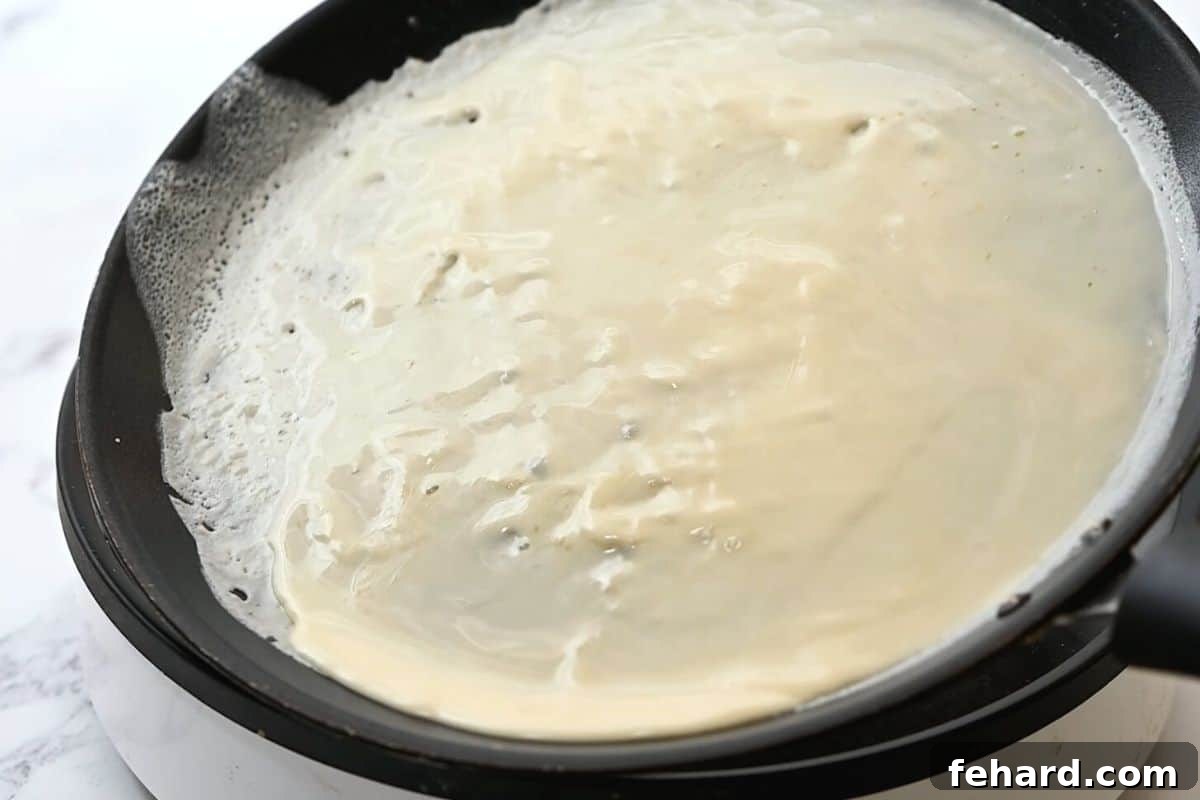 A hot skillet being tilted to evenly spread a thin layer of crepe batter across its surface.