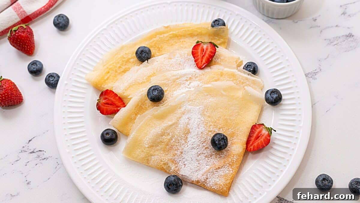 A vibrant display of freshly made crepes artfully arranged on a white plate, generously topped with an assortment of colorful fresh berries, creating an enticing sweet presentation.