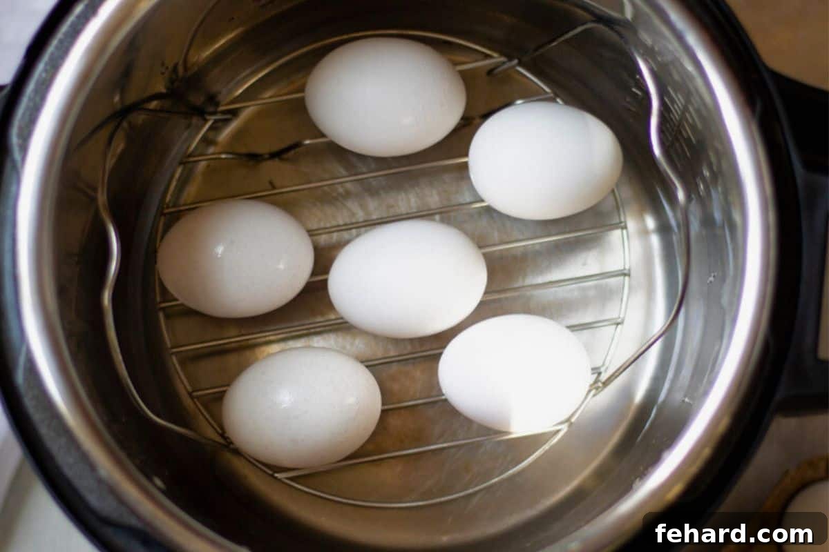 Five eggs resting on a metal trivet over water inside the inner pot of a pressure cooker, positioned for cooking.
