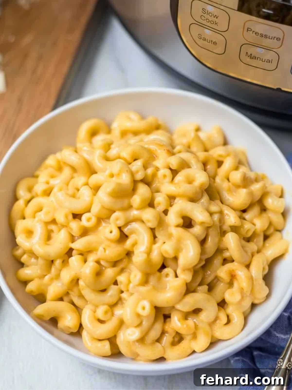 A steaming bowl of creamy, cheesy Instant Pot Macaroni and Cheese, perfectly garnished, sits invitingly next to a modern pressure cooker on a rustic wooden surface.