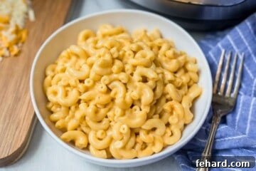 Instant Pot Mac and Cheese in white bowl next to cutting board with grated cheese and pressure cooker in background.