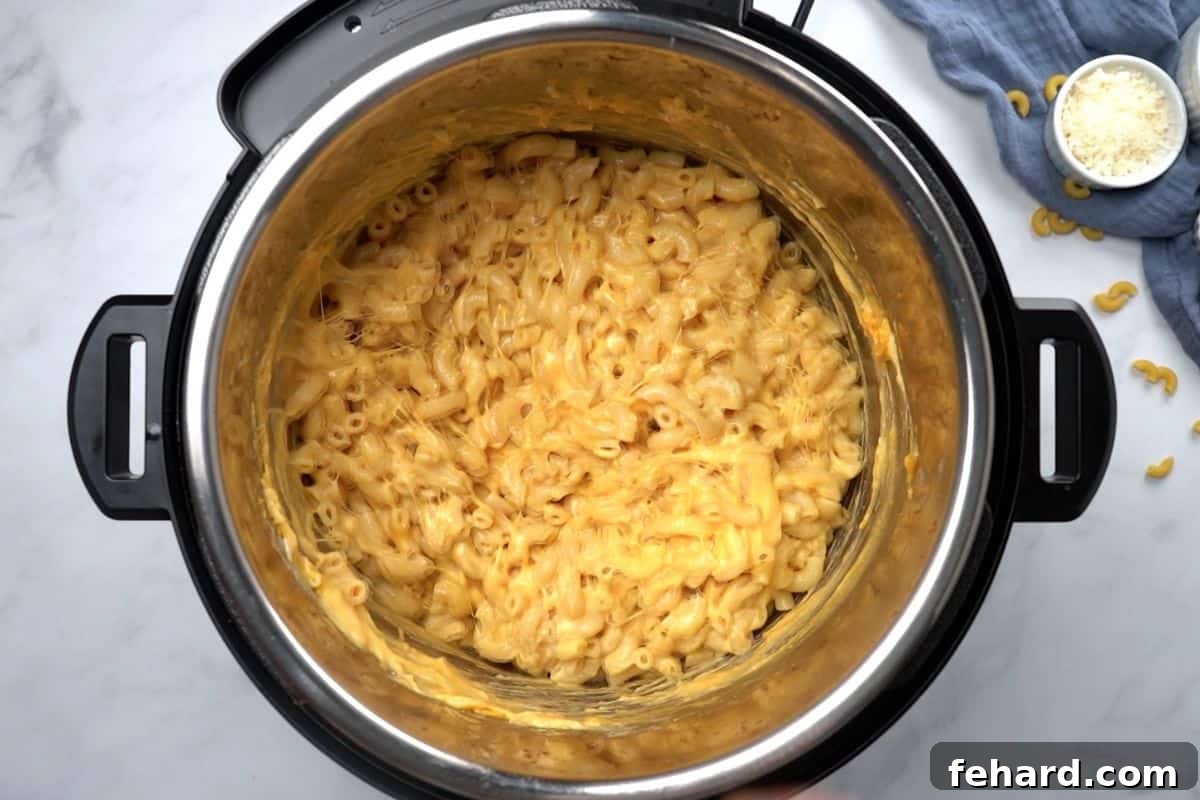 A close-up view of rich, creamy macaroni and cheese, freshly prepared, being stirred inside the inner pot of an electric pressure cooker, highlighting its smooth texture.