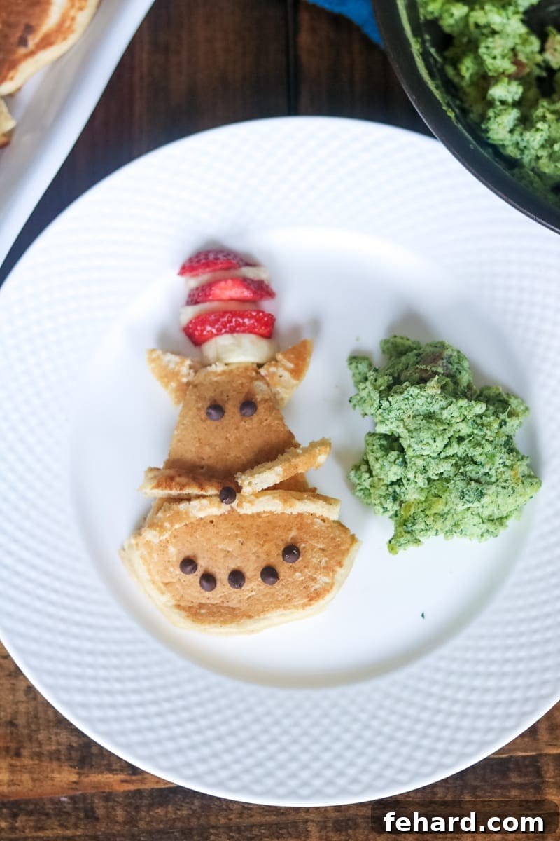Dr. Seuss Snacks and Breakfast Ideas A charming white plate featuring Cat in the Hat pancakes artfully decorated with fruit, alongside vibrant green eggs and savory ham, perfect for Dr. Seuss themed celebrations and Read Across America Day.