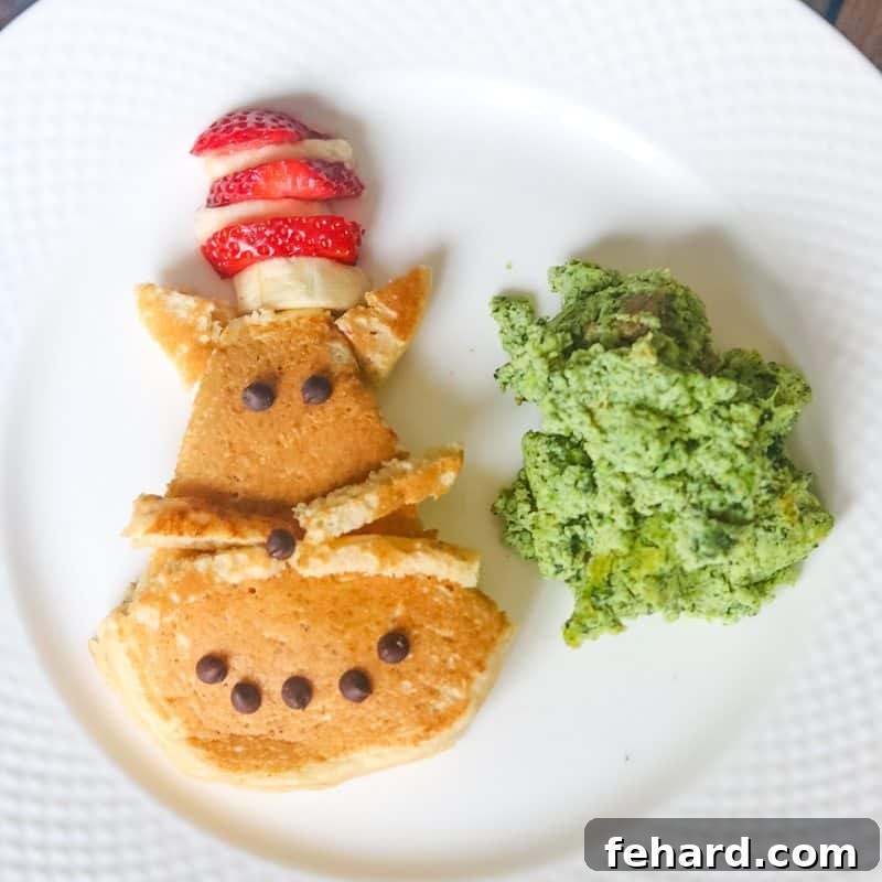 Creative Cat in the Hat Pancake Art for Kids Close-up of a delightful Cat in the Hat pancake, artfully decorated with fruit and chocolate chips, served with naturally green eggs and ham, ideal for Dr. Seuss Day.