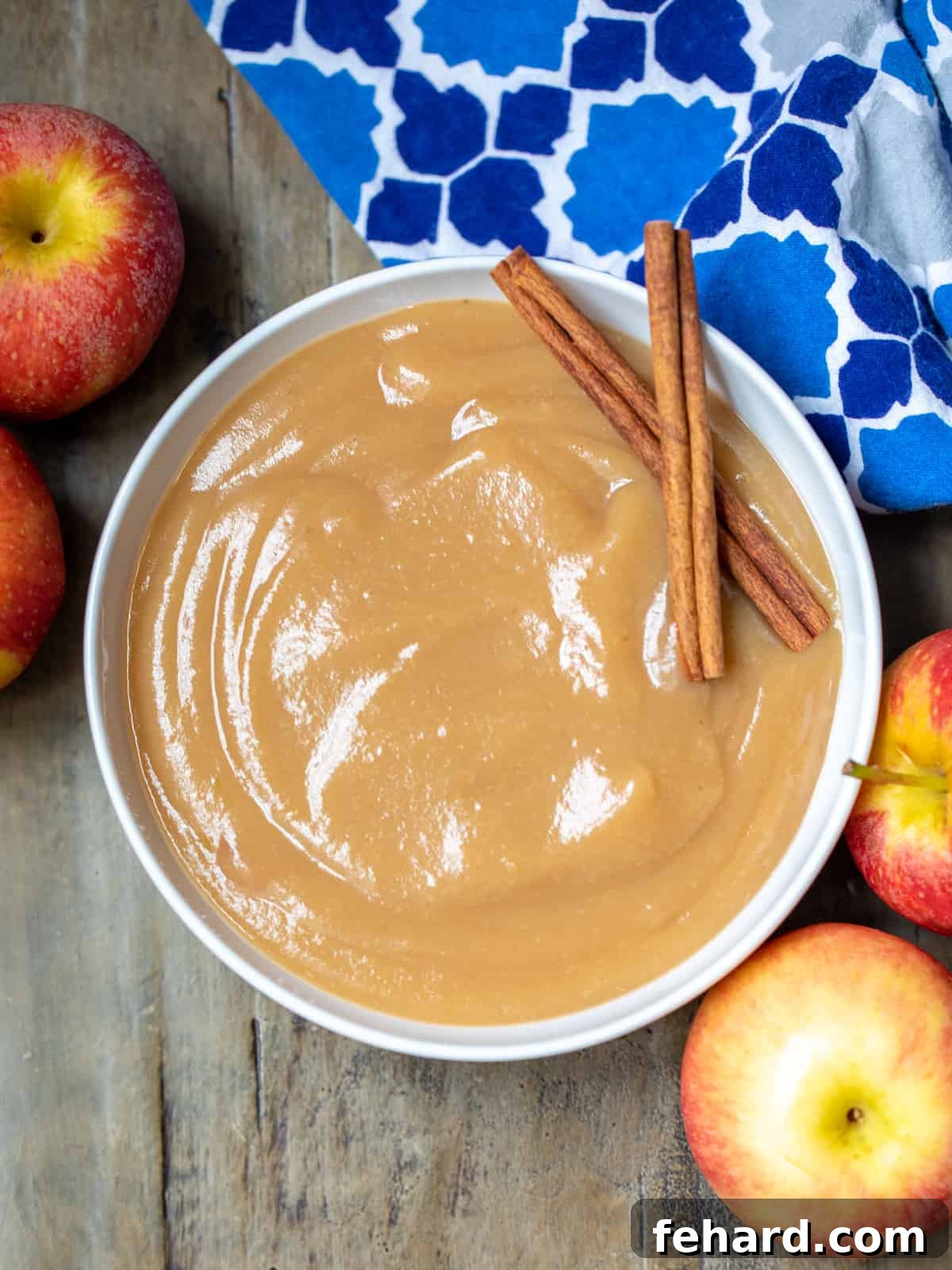Best Homemade Applesauce Recipe A charming bowl of freshly made homemade applesauce, beautifully garnished with aromatic cinnamon sticks, thoughtfully placed next to a selection of vibrant, fresh whole apples.
