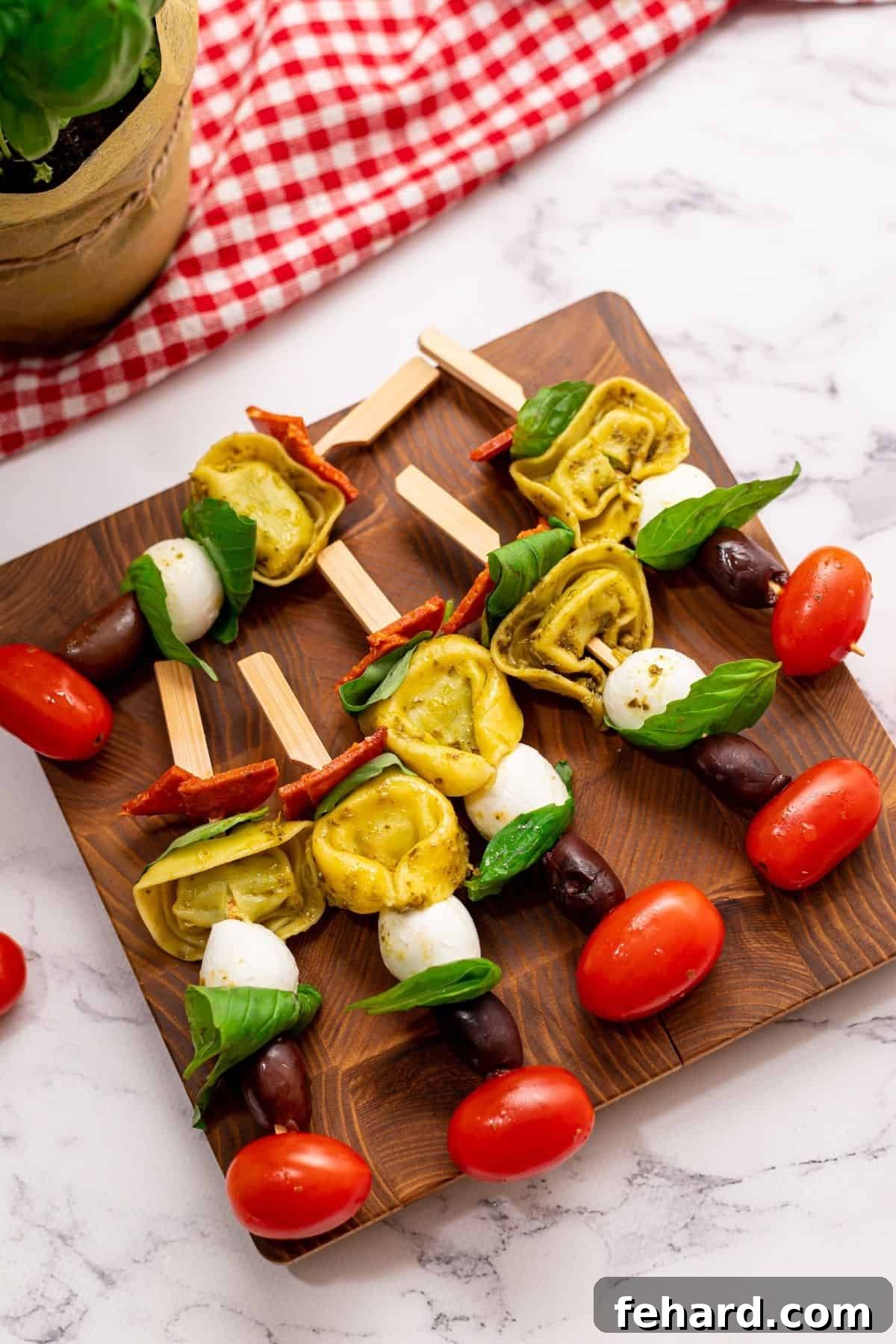 Appetizer sticks with cherry tomatoes, tortellini, basil, mozzarella and pepperoni on wooden cutting board.
