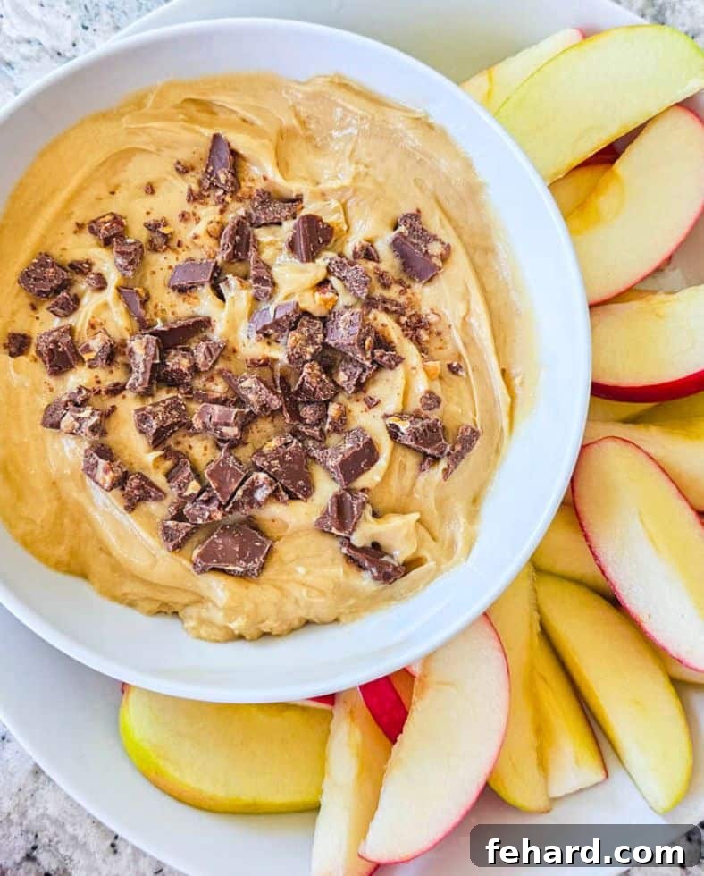 Cream Cheese Apple Dip Recipe Rich and creamy Cream Cheese Apple Dip in a white serving dish, garnished with chopped toffee bar bits, surrounded by perfectly sliced fresh apples.