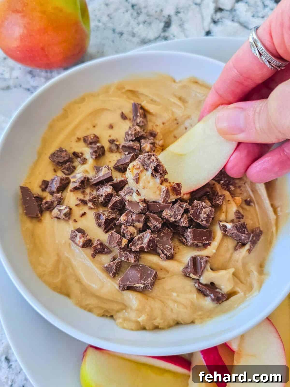 Easy Apple Dip Recipe for Parties A crisp apple slice being dipped into a rich, brown sugar cream cheese dip, showcasing its creamy texture.