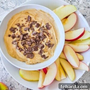 Cream Cheese Apple Dip in white dish topped with chopped toffee bar and served with sliced apples on the side.