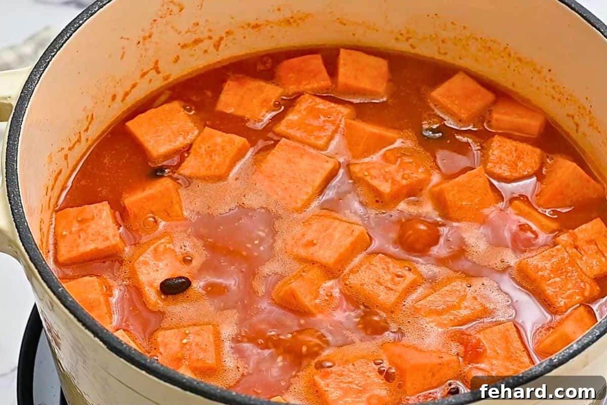 Simmering Sweet Potato Black Bean Chili Sweet potato chili gently simmering in a large soup pan, with quinoa and black beans visible, indicating a rich and tender texture developing.