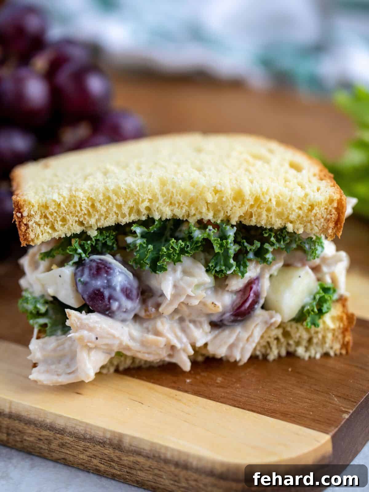 Chicken Salad with grapes, apples, and celery on thick white bread topped with curly kale on cutting board.