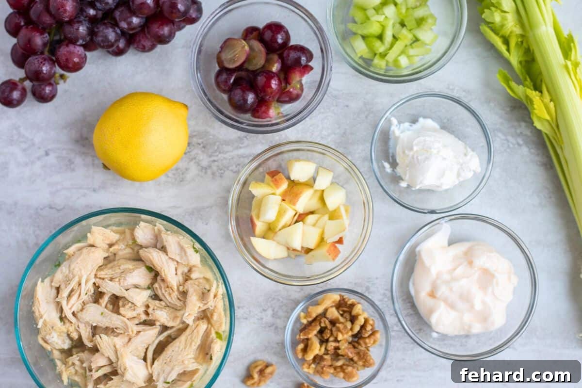 Ingredients for chicken salad on counter showing shredded chicken, walnuts, lemon, grapes, apples, yogurt, and mayonnaise
