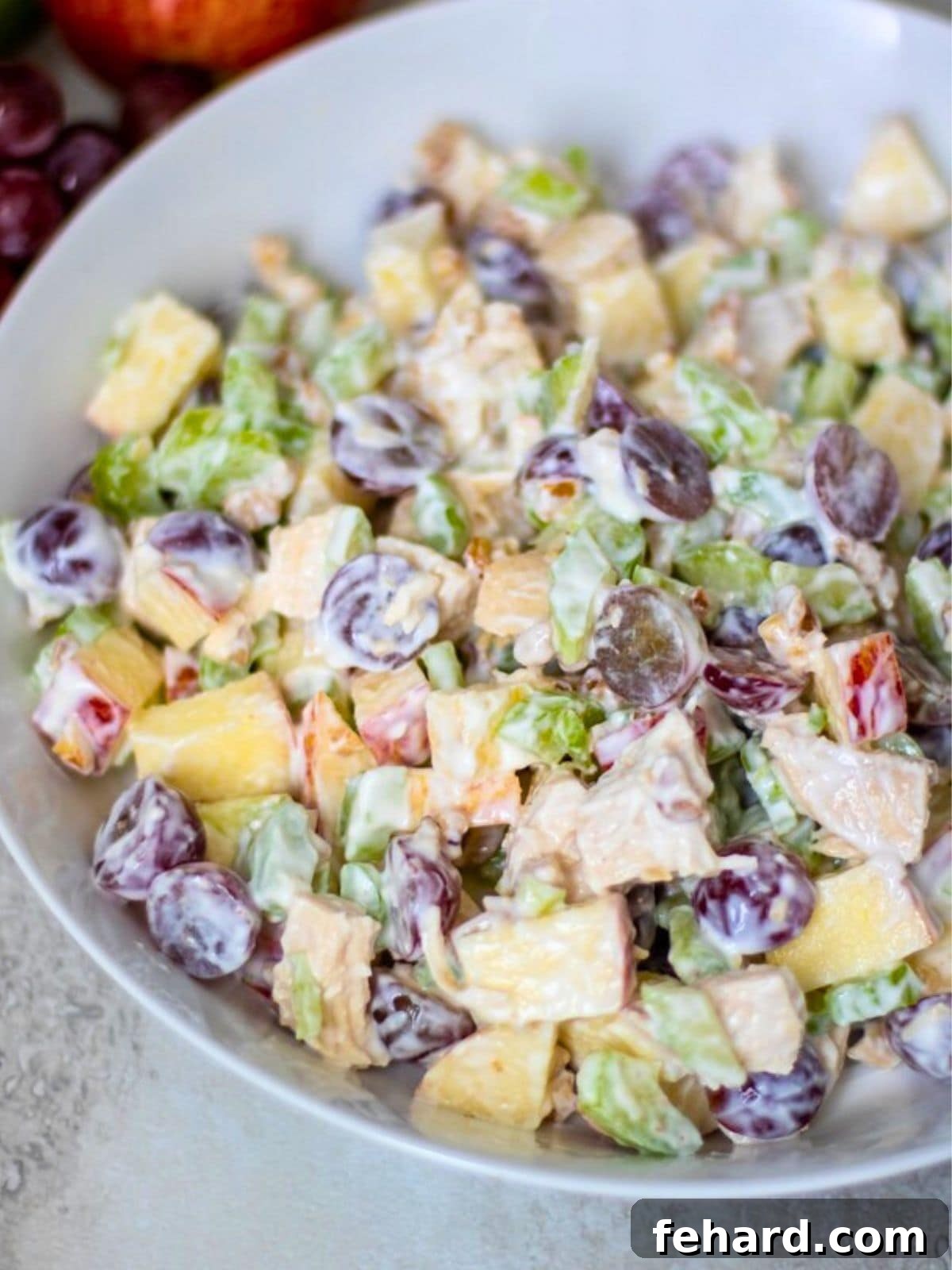 Chicken, apples, celery, grapes, and nuts combined with creamy dressing in mixing bowl.