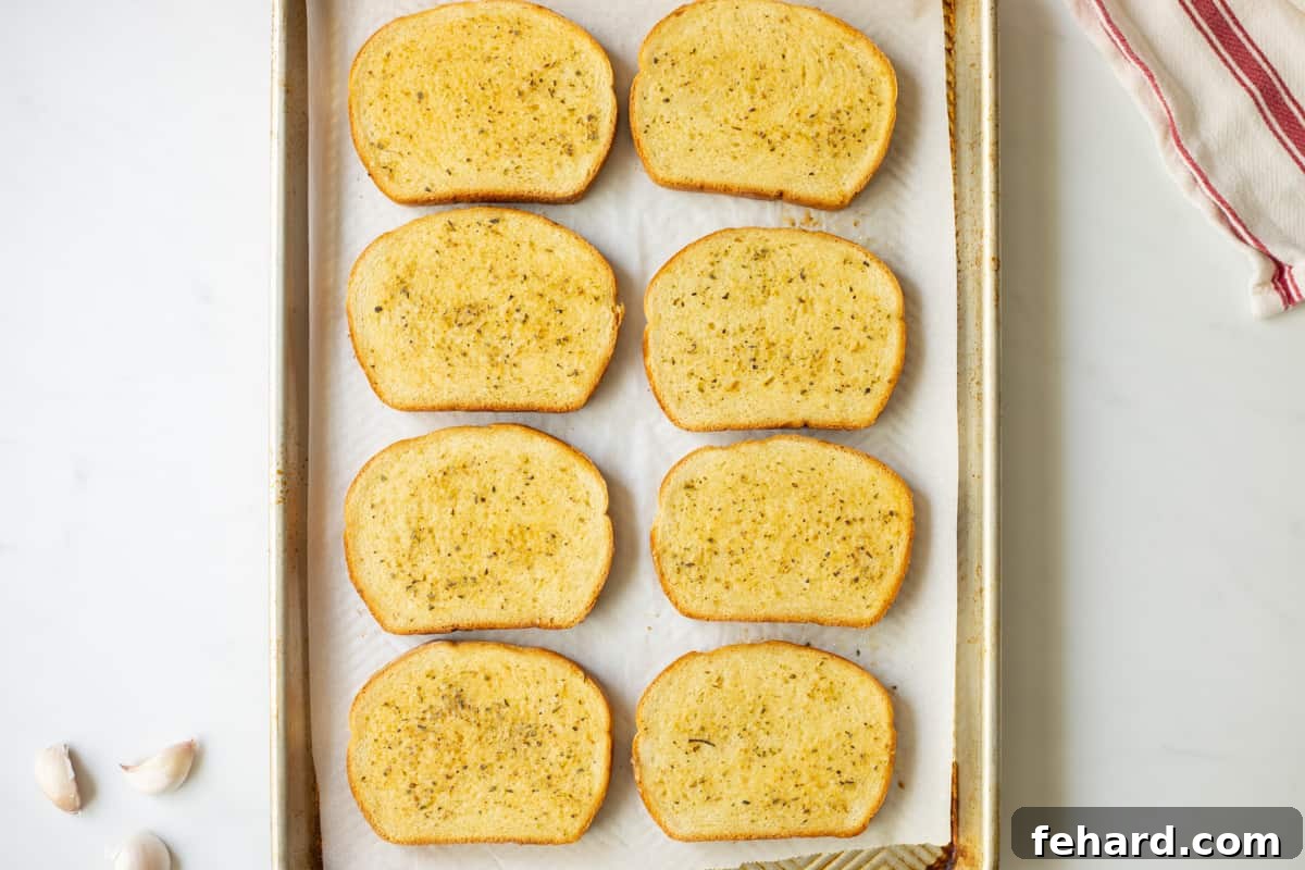 Perfectly toasted garlic toast on a sheet pan, ready to serve, with fresh garlic cloves nearby.