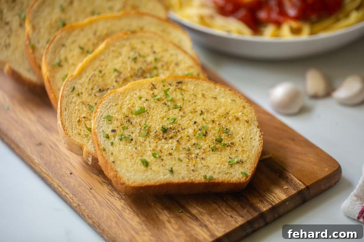Homemade Garlic Toast on a wooden cutting board with pasta in the background, ready for dinner.