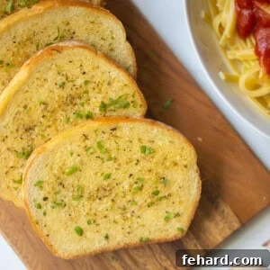 Homemade Garlic Toast on wooden cutting board with pasta in background.