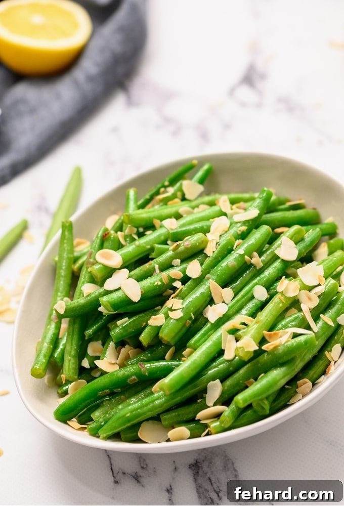 A serving dish filled with perfectly cooked Green Beans Almondine, garnished with toasted almonds and fresh lemon slices.