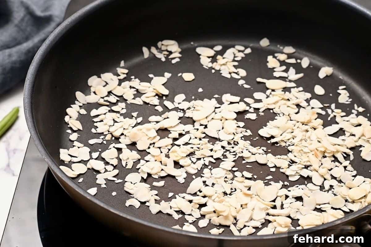 Slivered almonds being toasted in a dry sauté pan over medium-low heat.