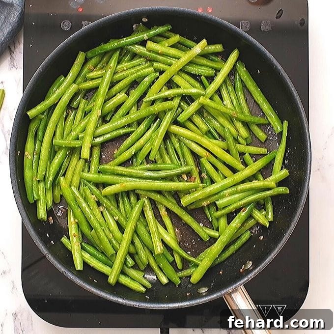 Green beans tossed in a skillet with lemon butter sauce, glistening and ready for serving.