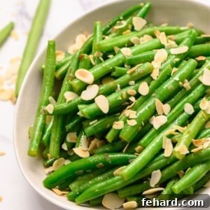 Bowl of green beans almondine topped with slivered almonds.