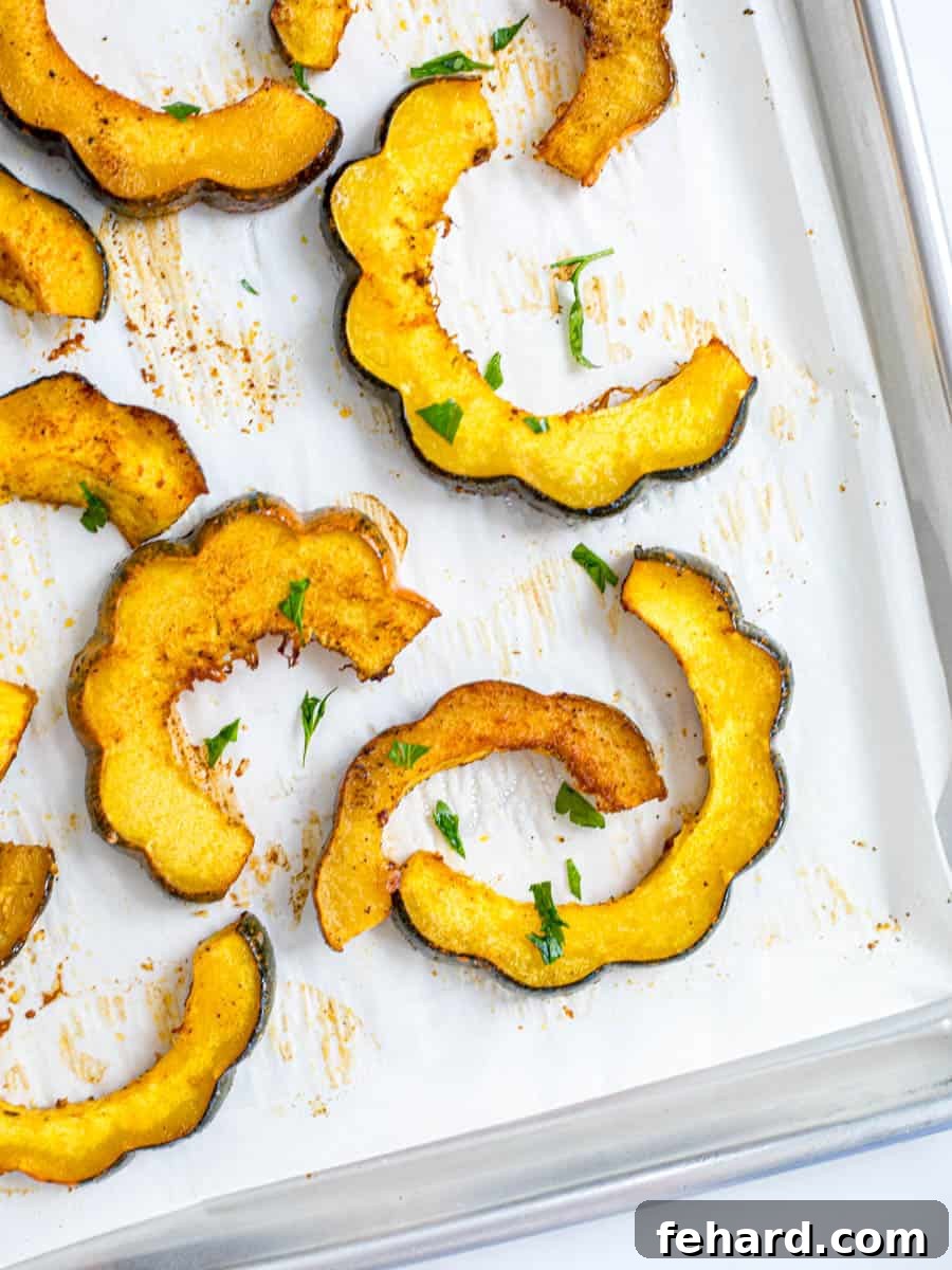 Slices of Roasted acorn squash on parchment paper topped with minced parsley.