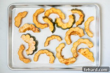 Seasoned slices of acorn squash on a slice of parchment paper on baking sheet.