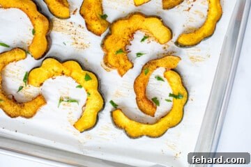 Slices of Roasted acorn squash on parchment paper topped with minced parsley.