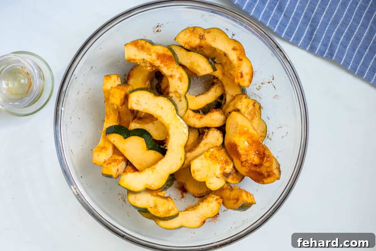 Sliced acorn squash in large mixing bowl tossed with olive oil, paprika, maple syrup, and salt.