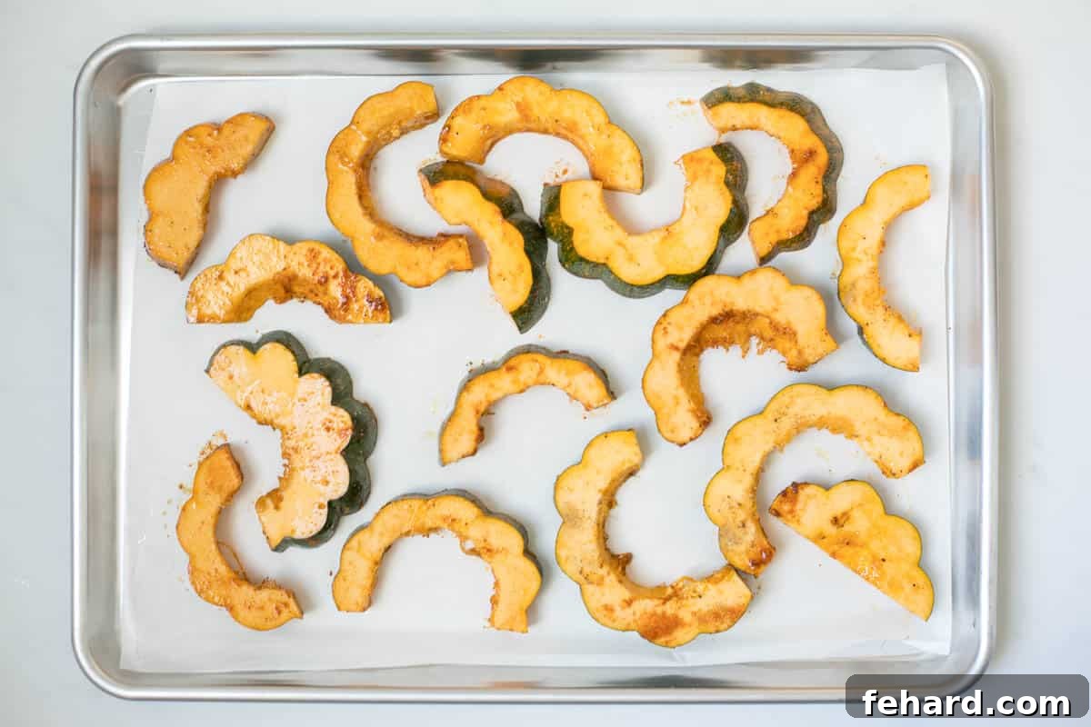Seasoned slices of acorn squash on a slice of parchment paper on baking sheet.