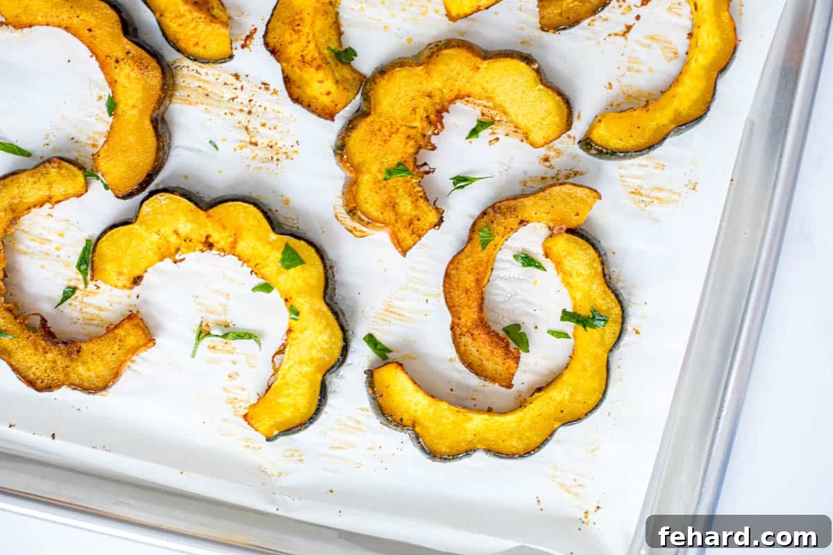 Slices of Roasted acorn squash on parchment paper topped with minced parsley.