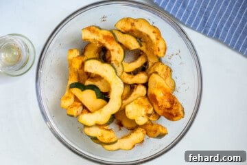 Sliced acorn squash in large mixing bowl tossed with olive oil, paprika, maple syrup, and salt.