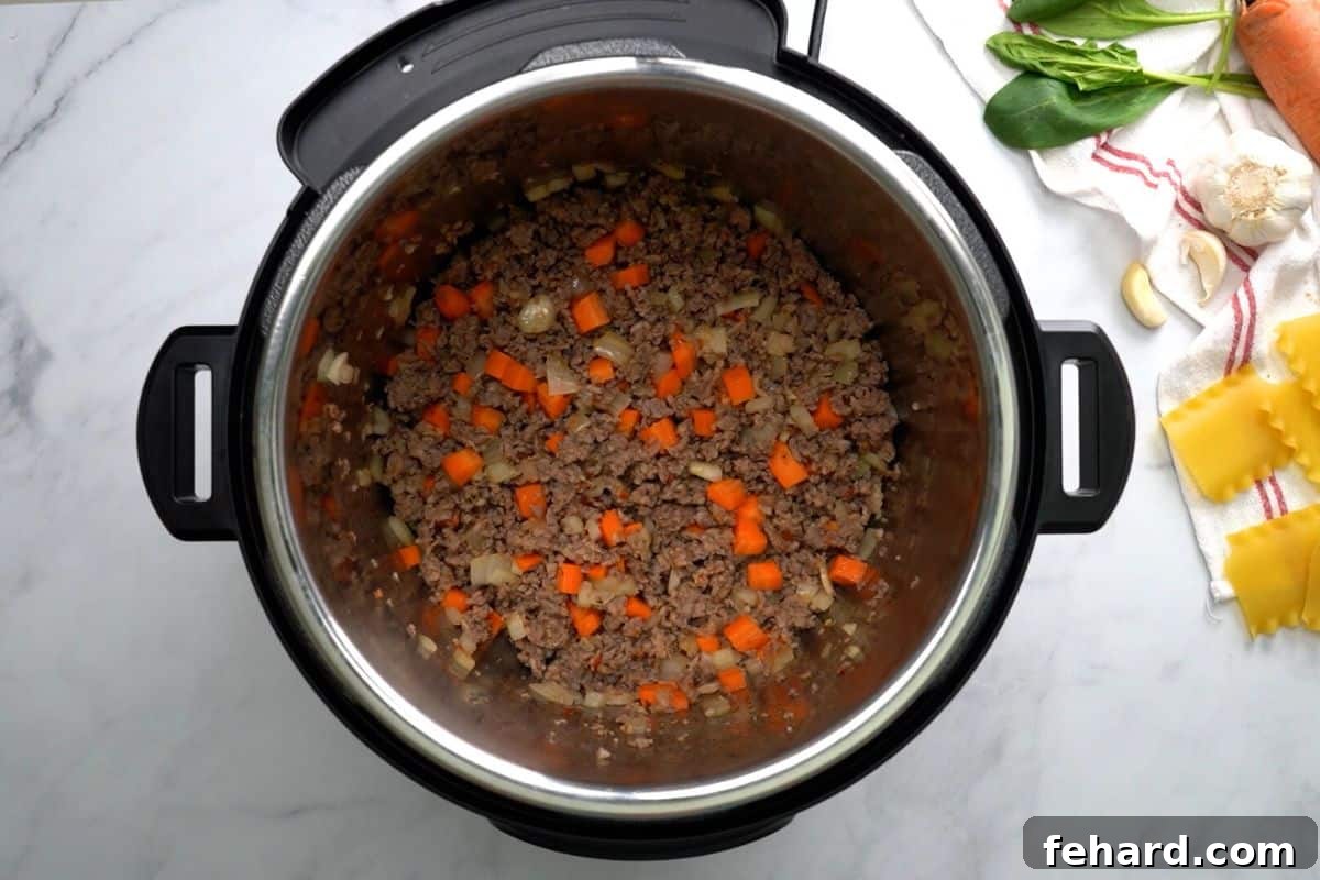 Ground Italian sausage, minced carrots, and diced onions are sautéed together in the Instant Pot's inner pot, creating a fragrant base for the lasagna soup recipe.