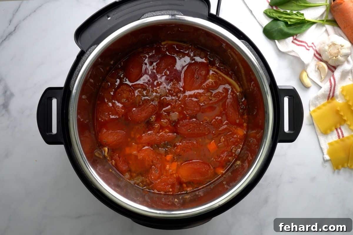 All the raw ingredients for Instant Pot Lasagna Soup, including broth, tomatoes, marinara, seasonings, and pasta, are carefully layered inside the Instant Pot before pressure cooking.