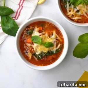 Instant Pot Lasagna Soup with sausage and spinach dished out in a white bowl topped with parmesan and mozzarella cheese.