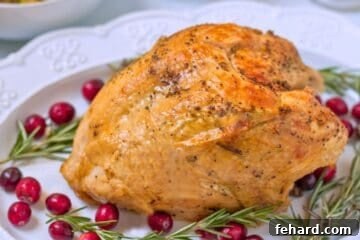Instant pot turkey breast on white platter with crispy skin surrounded by rosemary sprigs and cranberries.